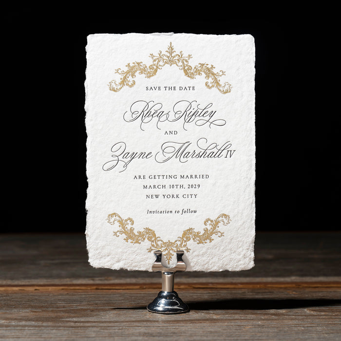 Rhea Save the Date card with ornate designs on a stand against a dark background