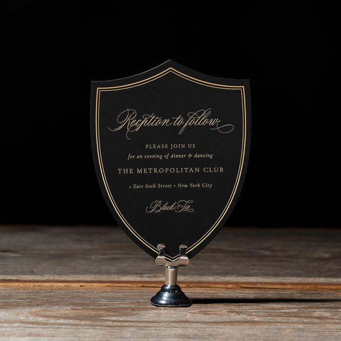 Rhea decorative black shield reception card with gold text on a wooden surface