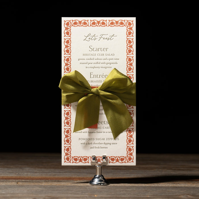 Royce menu card with a green bow on a stand against a black background