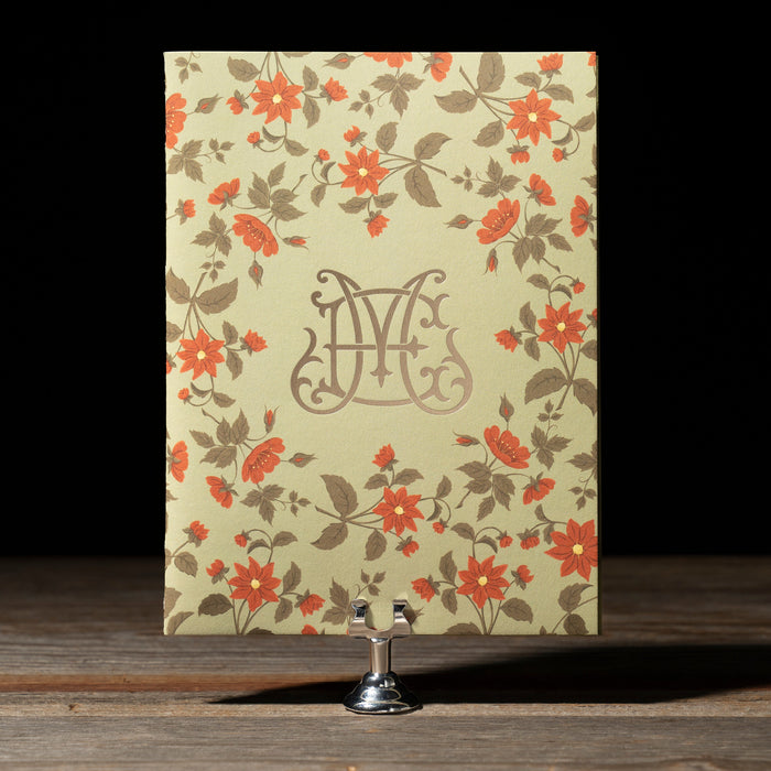 Floral patterned book-style Royce wedding invitation with a monogram on a wooden surface