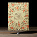Floral patterned book-style Royce wedding invitation with a monogram on a wooden surface