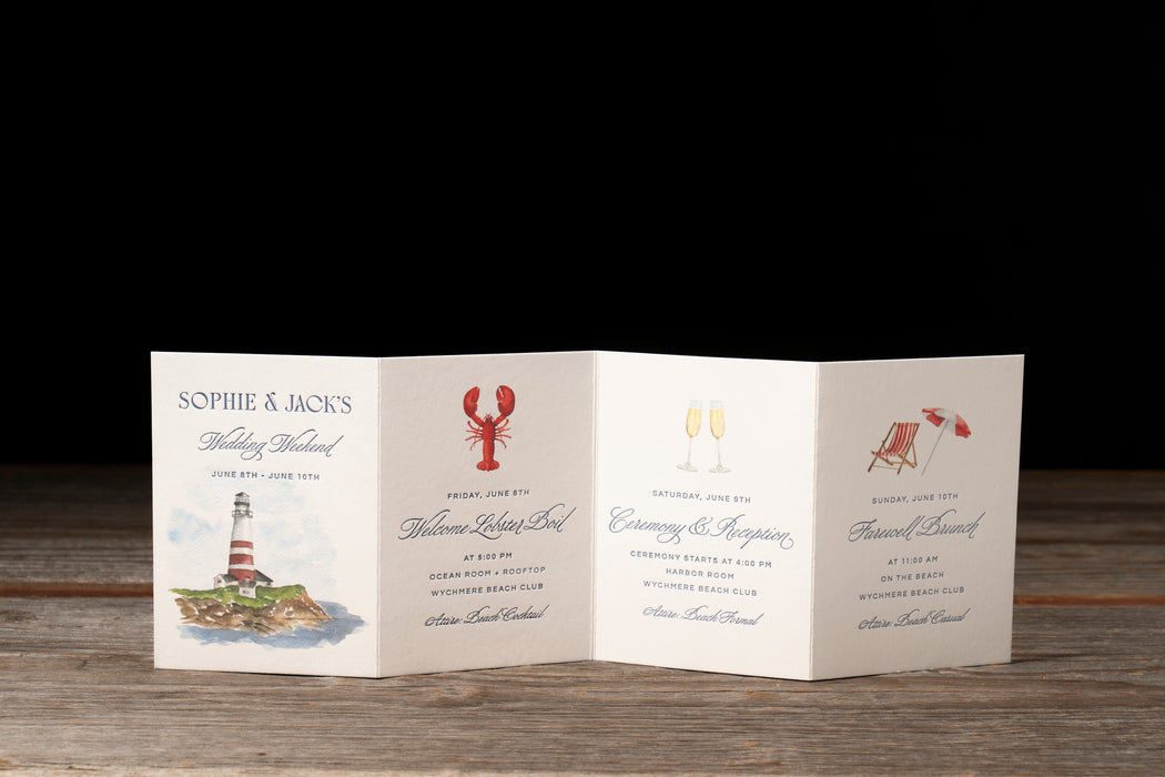 Folded wedding invitation events card with nautical-themed illustrations on a wooden surface.