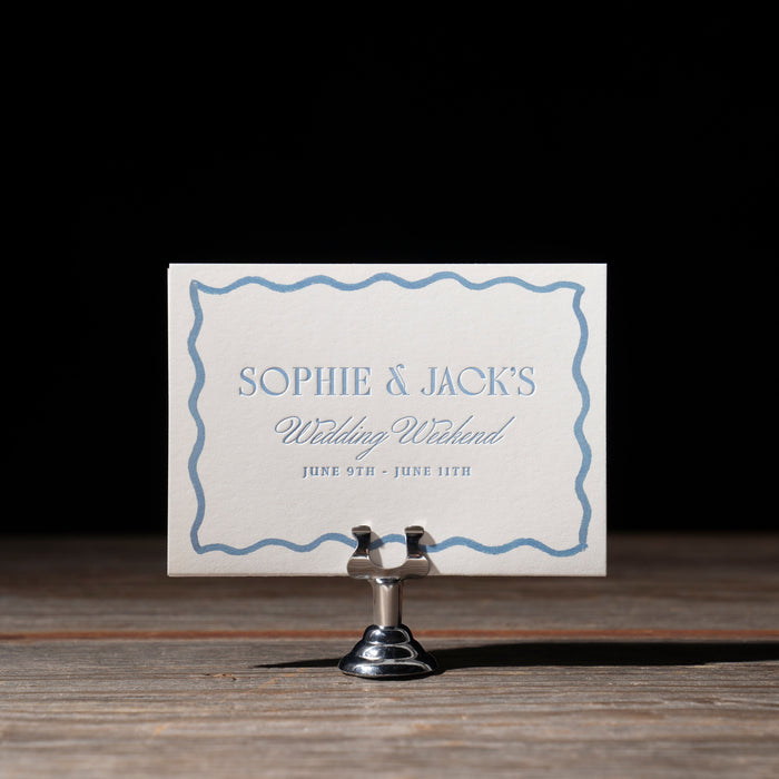 Event's Card with 'Sophie & Jack's Wedding Weekend' on a stand against a dark background