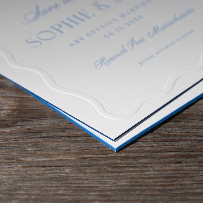 Ryann wedding invitation card and save the date card with blue edgepaint border on a wooden surface