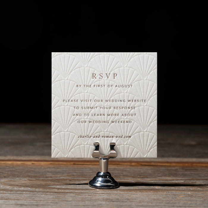 White debossed RSVP card on a wooden stand with a dark background