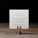 White debossed RSVP card on a wooden stand with a dark background