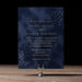 Navy blue wedding invitation with gold text on a wooden surface and black background