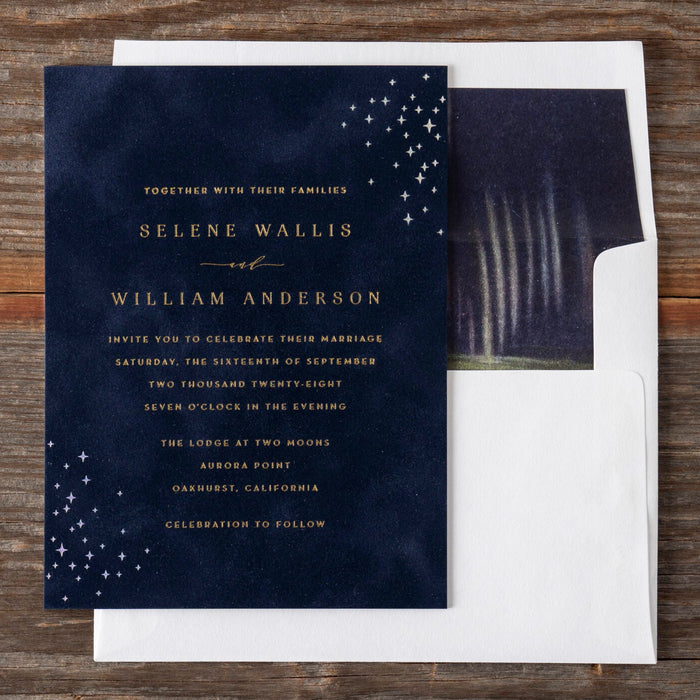 Navy blue Selene wedding invitation with gold text on a wooden surface