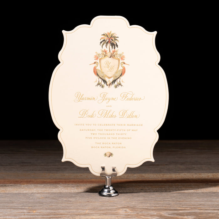Yasmin wedding invitation with tropical crest on a stand against dark background